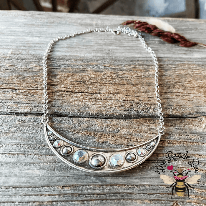 A silver-colored necklace with a crescent moon and star design, displayed against a rustic wooden background with a bug zapper light in the background, indicating it might be a decorative piece.