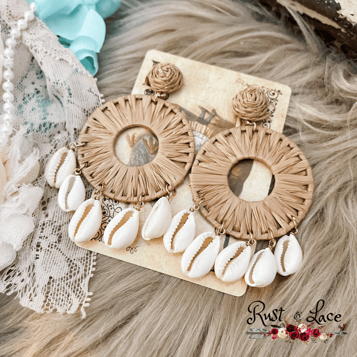 A pair of beige raffia shell earrings with white and brown accents, displayed against a lacy background.
